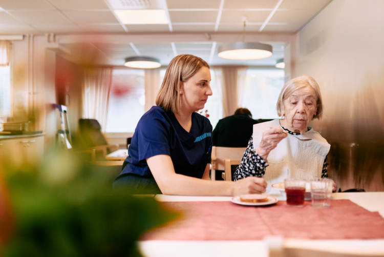 Hoitaja auttaa iäkästä asukasta syömään palvelutalossa.