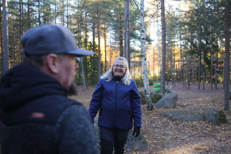 Erja Kinnunen katsoo kameraan hymyillen, etualalla on Sami Kinnusen hahmo sumeana. Molemmat seisovat leikkipuistossa. 